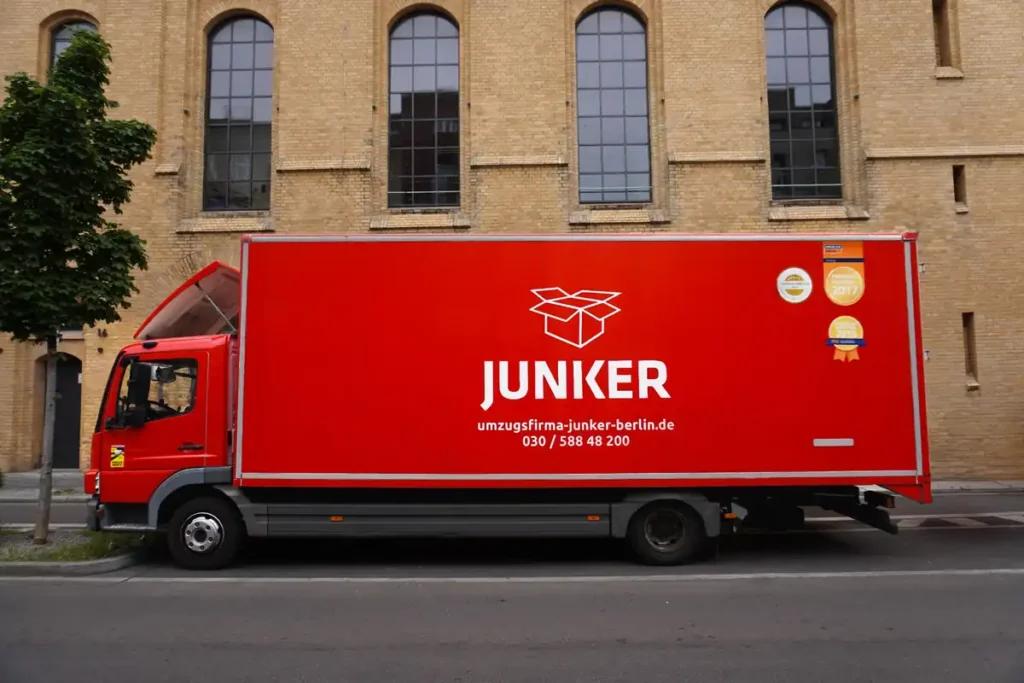 Roter Umzugs-LKW der Umzugsfirma Junker Berlin mit Auszeichnungen, geparkt vor einem Gebäude