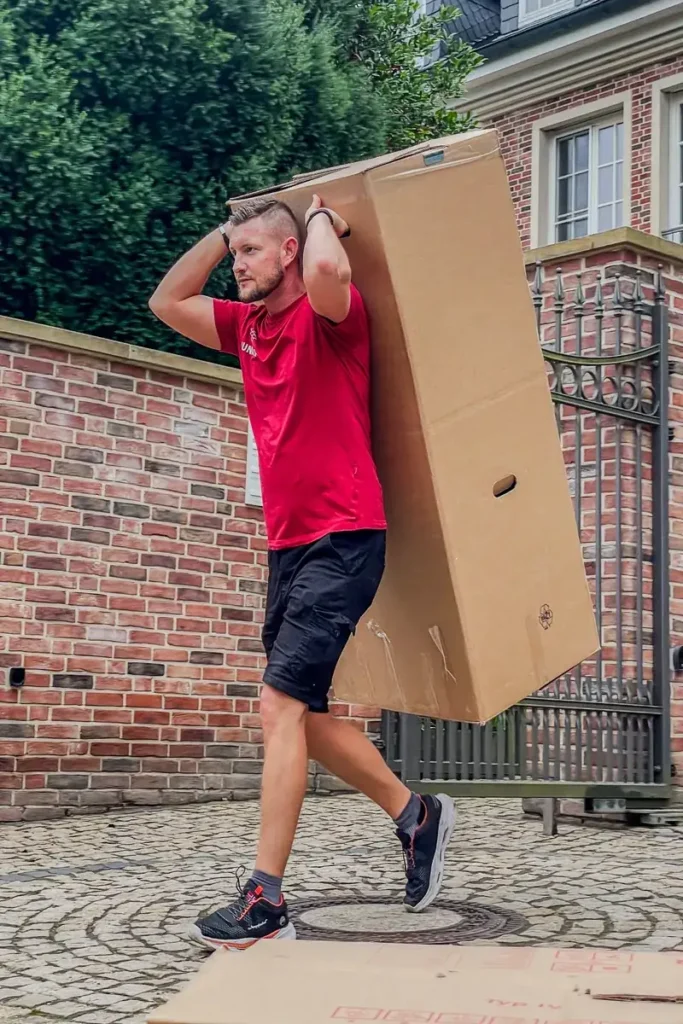 Umzugshelfer der Umzugsfirma Junker trägt einen großen Umzugskarton beim Möbeltransport.