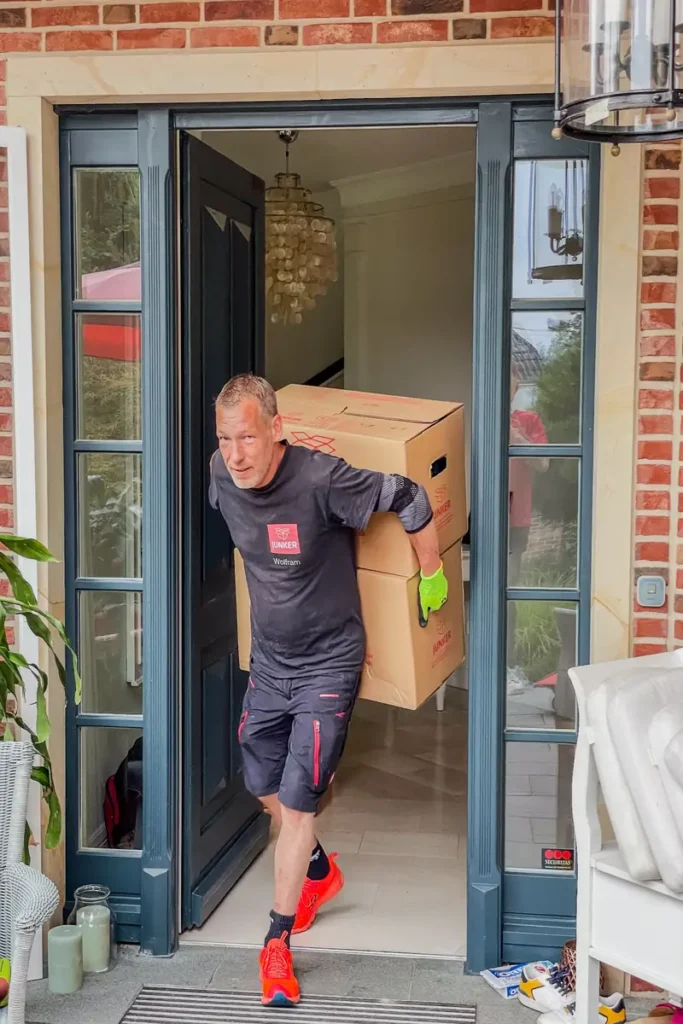 Umzugshelfer der Umzugsfirma Junker trägt zwei Umzugskartons beim Wohnungsumzug.