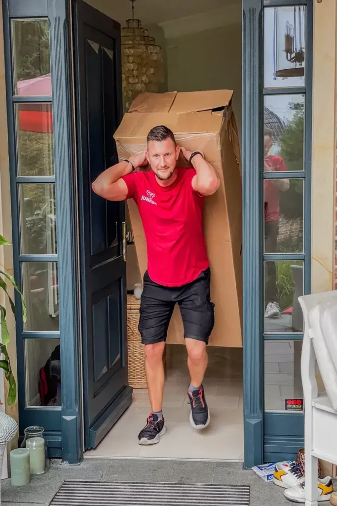 Mitarbeiter der Umzugsfirma Junker trägt einen Umzugskarton aus dem Haus – professioneller Möbeltransport mit Sorgfalt.