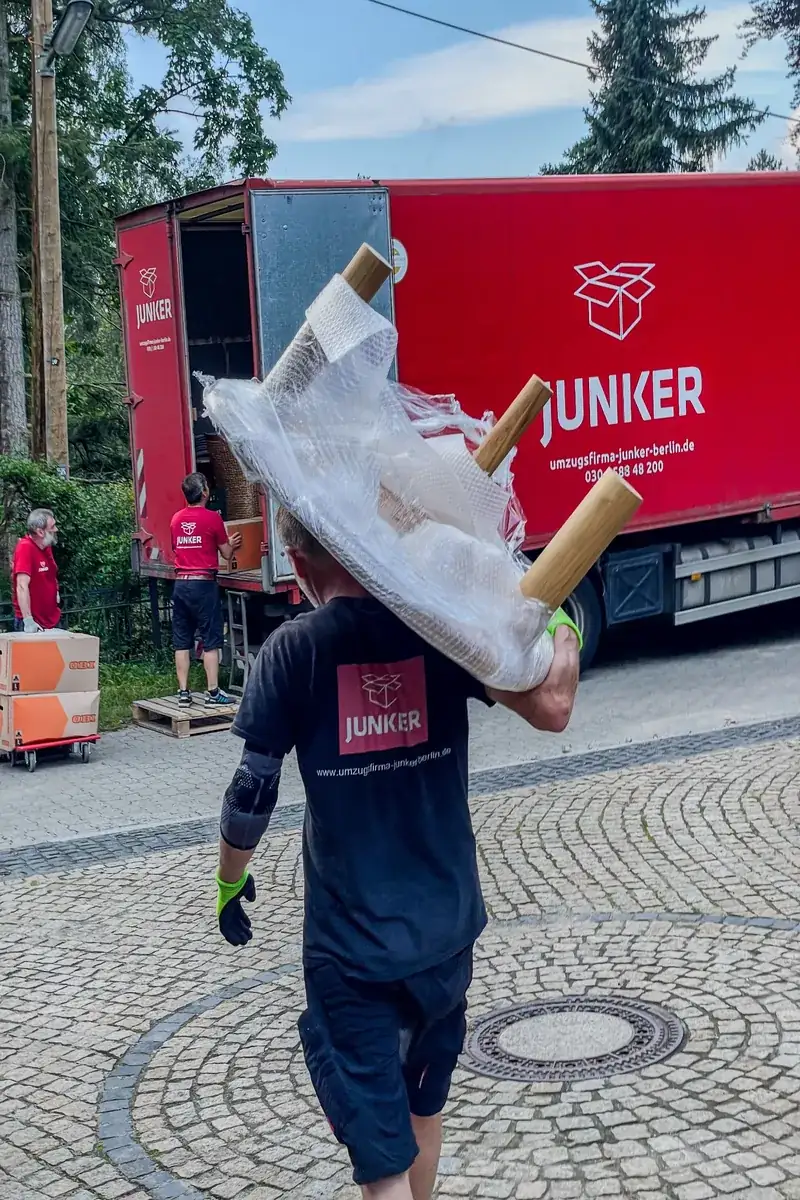 Umzugshelfer der Umzugsfirma Junker trägt verpackte Möbel zum Lkw – professioneller Transport mit Sorgfalt.