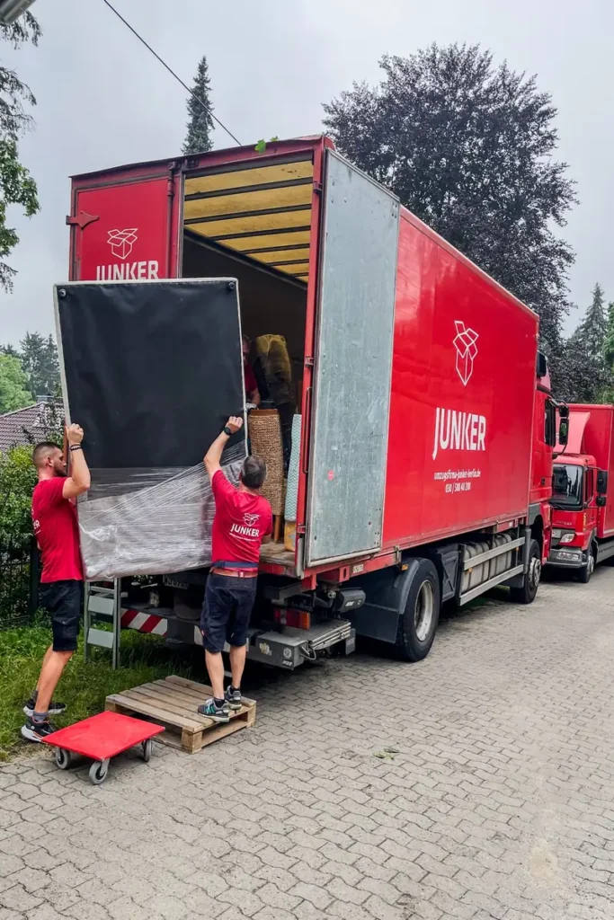 Umzugshelfer der Umzugsfirma Junker laden Möbel in einen roten Junker-Lkw – professioneller Transportservice.