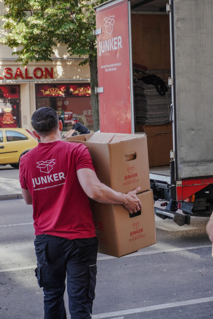 Mitarbeiter der Junker Umzugsfirma trägt zwei Umzugskartons in einen Umzugswagen.